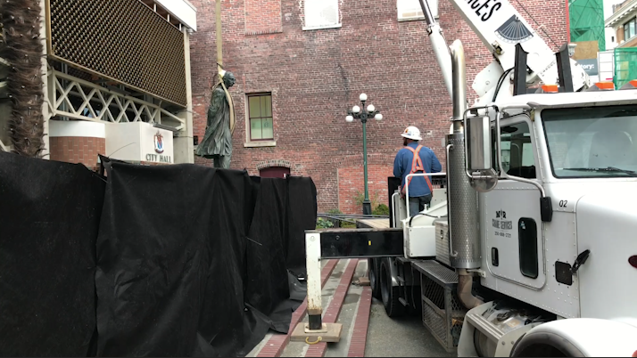 The statue being removed by a crane truck