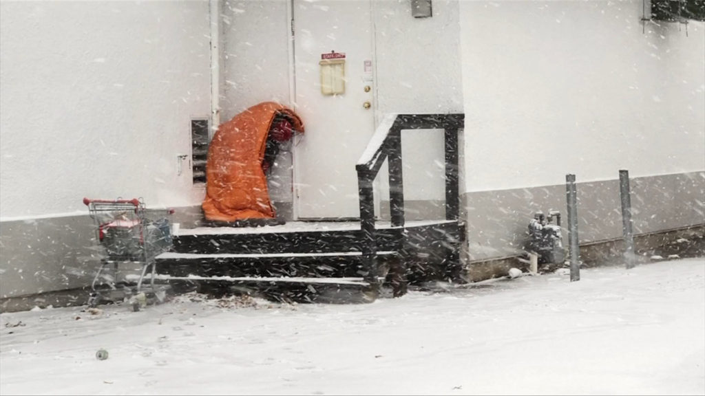 A homeless person huddles in a sleeping bag on the back steps of a modular building to keep warm in the Oceanside community of Parksville